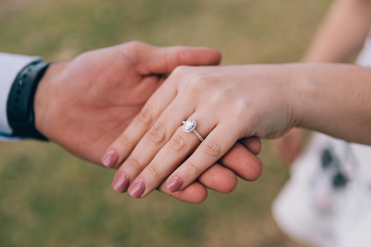 a male hand touching a female hand with a propousal ring